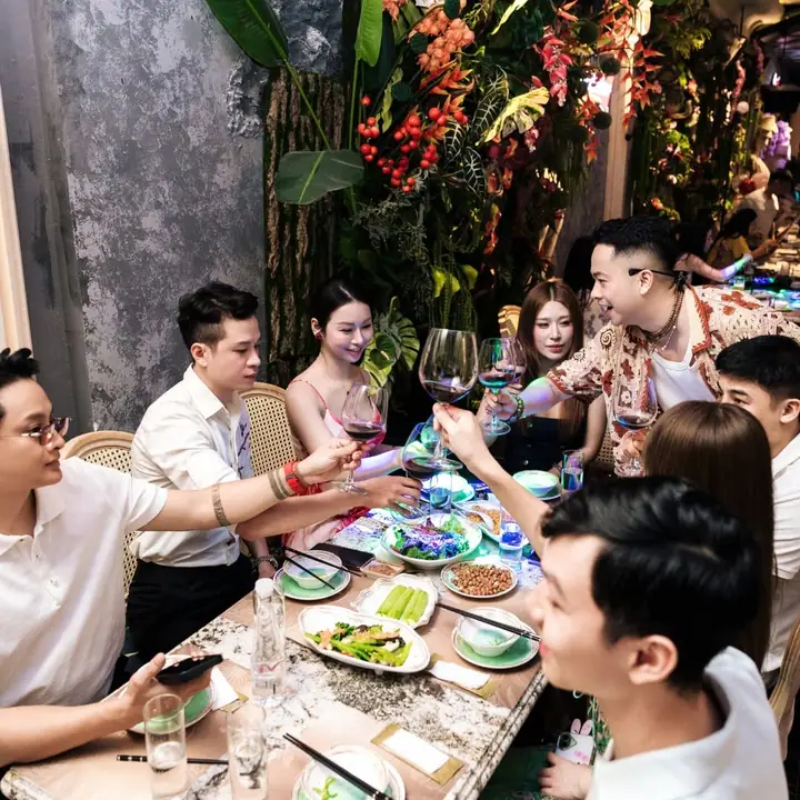Nhóm bạn quây quần bên bàn tiệc cạnh vách hoa